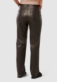 Pantalons en cuir marron avec un design à jambe droite, présentant une taille haute, des poches arrière et une texture lisse. Chaussures noires plates portées.