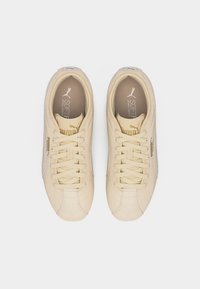 Ζευγάρι μπεζ αθλητικά παπούτσια Puma με μαλακό αφρό και κορδόνια, σε θέα από πάνω σε απλό λευκό φόντο.