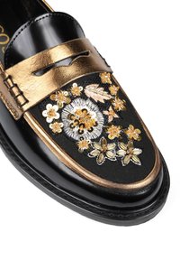 Czarne skórzane mokasyny z metaliczną złotą paskiem, zdobione misternym florystycznym haftem w odcieniach złota i srebra na fakturowanej czarnej powierzchni.