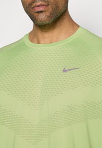 Ανοιχτό πράσινο αθλητικό μπλουζάκι Nike με στρογγυλή λαιμόκοψη, που διαθέτει υφή και μικρό μωβ λογότυπο Nike στο στήθος.
