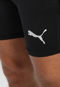 Sorte athletic shorts laget av elastisk materiale, med en hvit Puma-logo nederst til venstre og en glatt, tettsittende design.
