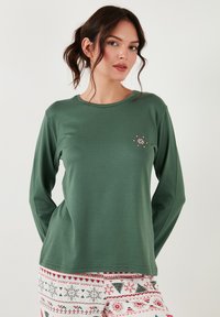 Cămașă verde cu mâneci lungi din material moale, cu guler rotund. Prezintă o broderie florală mică pe piept.