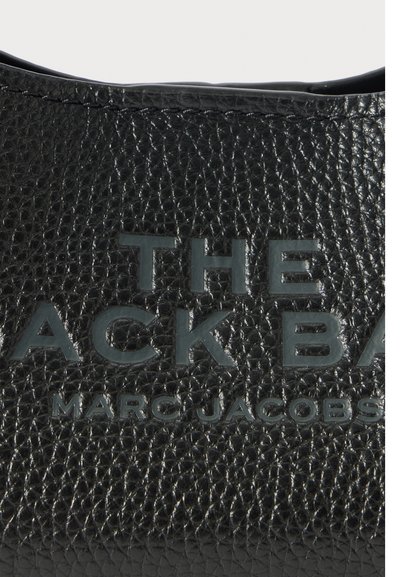 Zwarte gestructureerde lederen oppervlakte met reliëftekst "THE BACK BAG MARC JACOBS" in vette hoofdletters.