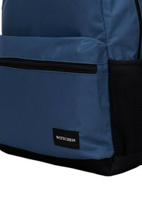 Zaino in nylon blu con tasca laterale in rete nera, compartimento frontale con zip e un'etichetta rettangolare nera con il logo "WITTCHEN".