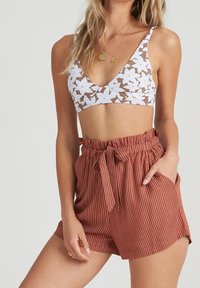 Top bikini bianco con motivo floreale, scollatura a V profonda e sfondo marrone; abbinato a pantaloncini a vita alta striati color ruggine con laccio.