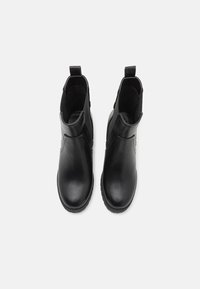 Paire de bottines noires en cuir avec bouts arrondis et languettes, vue de dessus sur fond blanc.