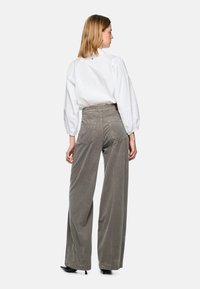 White puff-sleeved blouse with button detail at the back, paired with high-waisted grey corduroy wide-leg pants and black heeled shoes.