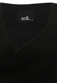 Vêtement noir avec un design avant superposé et une étiquette de la marque adL en taille moyenne à l'intérieur de l'encolure.