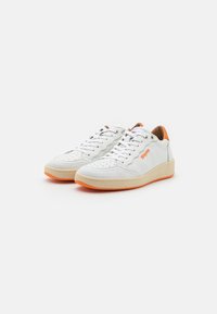 Baskets en cuir blanc avec des accents orange et une semelle beige. Les caractéristiques incluent un bout perforé, des lacets plats et une languette rembourrée.