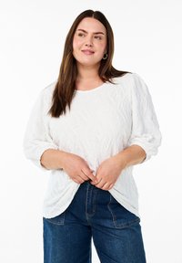 Hvid struktureret bluse med puffede ærmer, rund halsudskæring og en afslappet pasform, parret med mørke denimjeans.