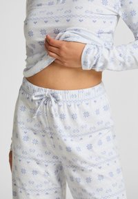 Koszula nocna z długimi rękawami i spodnie z regulowanym paskiem w jasnoniebieskim materiale, zdobione wzorem śnieżynek i serc w ciemniejszych odcieniach niebieskiego.