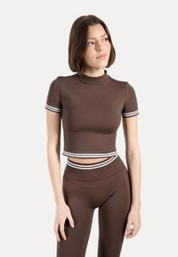 Brązowy krótki top z krótkimi rękawami i wysokim dekoltem, z białymi paskami na rękawach i dolnym brzegu. Materiał wydaje się rozciągliwy.