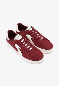 Zapatillas de ante marrón con acentos blancos, que presentan cordones planos, una suela de goma y un parche de logo en la lengüeta.