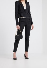 Černý peplum blazer přes krémový top, doplněný těsnými černými kalhotami. Doplňky zahrnují malou černou kabelku s řetízkovým popruhem.