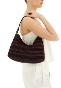 Borsa in tessuto bordeaux con strisce orizzontali, fondo in pelle liscia e una singola tracolla, tenuta da una persona.