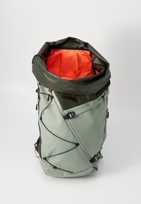 Grønn ryggsekk med oransje innvendig, rull-topplukking, justerbare stropper og elastiske bungee-snorer for oppbevaring. Holdbar tekstur.