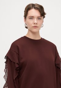  camisola bordô de manga longa com detalhes em renda nas mangas, decote redondo e um tecido suave e texturizado.