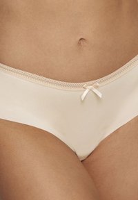 Slips in cotone beige con un delicato bordo in pizzo e un piccolo fiocco in satin al centro davanti, caratterizzati da una texture liscia e un design aderente.