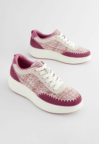 Violetti ja beige lenkkarit, joissa on teksturoitu kangaspäällinen, nauhakiristys ja paksu valkoinen pohja. Sisältää koristeompeleet ja vaaleanpunaiset yksityiskohdat.