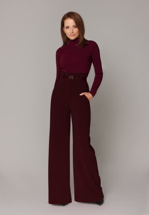 Bordowy long-sleeve top połączony z szerokimi, bordowymi spodniami z paskiem w talii. Materiał ma gładką teksturę. Czarne szpilki dopełniają całość.