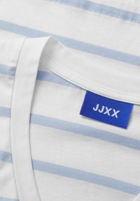 Camiseta de algodón blanca con rayas horizontales azul claro, con una etiqueta azul que dice "JJXX" en blanco, cuello redondo y textura suave.