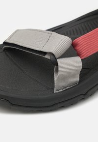 Black sandal with a textured rubber sole, featuring a grey adjustable strap and a pink accent strap, crafted from durable materials.