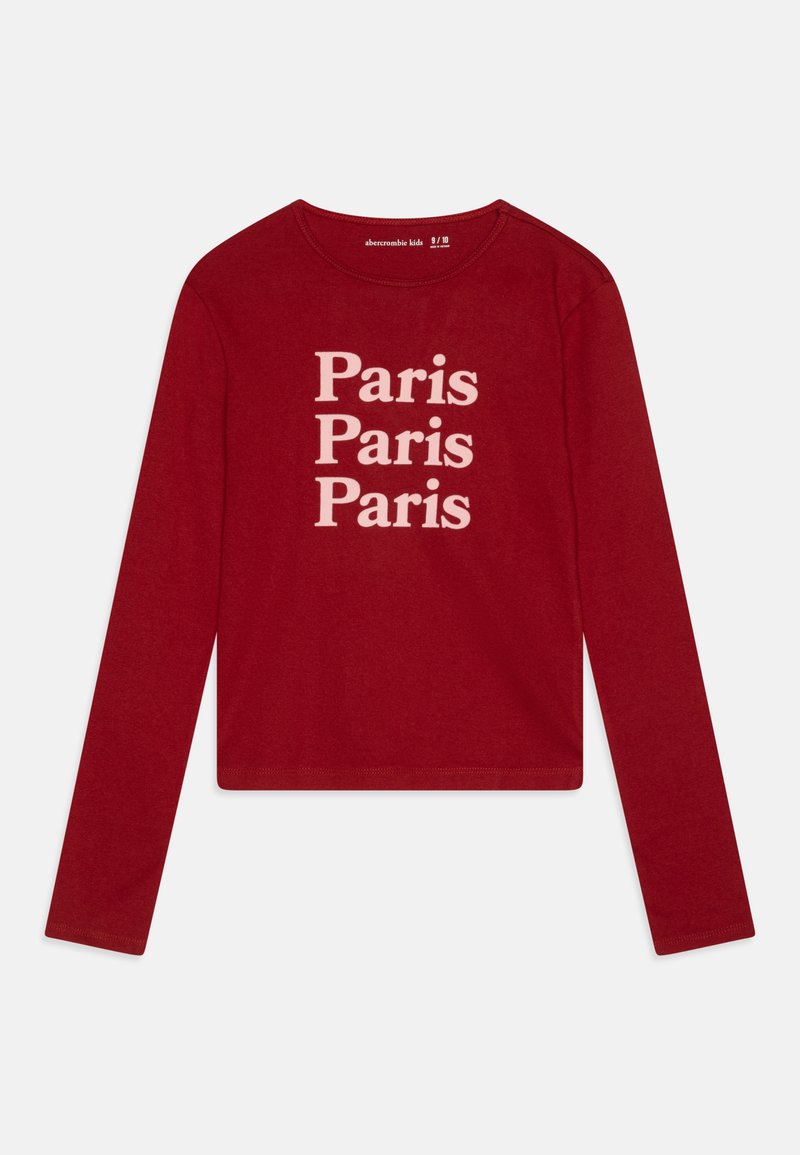 Chemise rouge à manches longues avec répétition du texte "Paris" en crème. Tissu lisse avec un col rond, design cropped et manches ajustées.