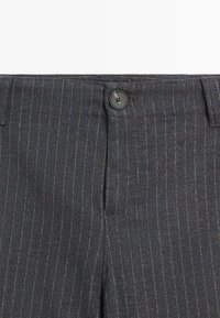 Pantaloni grigi scuri con righe verticali, dotati di chiusura frontale con bottone, passanti per cintura e una texture di tessuto liscia.