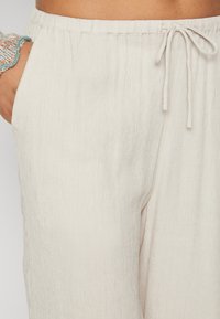Světle béžové kalhoty s jemně zvrásněnou texturou, vybavené elastickým pasem a šňůrkou na stažení, s bočními kapsami.