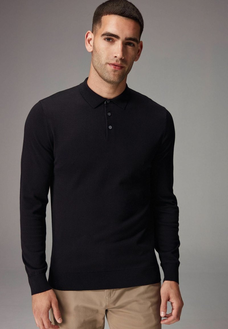 Camisa polo negra de manga larga con cuello acanalado, tapeta de tres botones y puños ajustados, hecha de un material de punto suave.