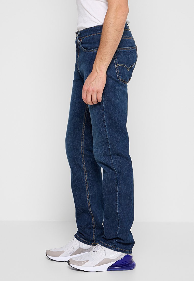 Dunkelblaue Denim-Jeans mit geradem Bein, ausgestattet mit orangen Nähten und vorderen Taschen. Getragen mit weißen und grauen Sneakers.