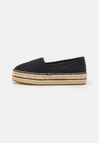 Espadrille negro sin cierre con parte superior texturizada, media suela de yute y costuras en negro contrastantes a lo largo de la suela. Diseño de perfil bajo.