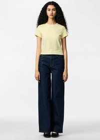 Żółty krótki t-shirt wykonany z bawełny; w zestawieniu z szerokimi, ciemnoniebieskimi dżinsami. Prosty krój z krótkimi rękawami i bez widocznych wzorów.