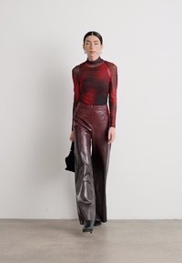 Transparante top met lange mouwen in een verloop van rood en zwart, gecombineerd met hoge taille burgundy leren broek met wijde pijpen en een kleine zwarte tas.