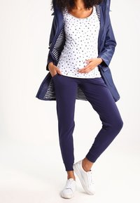 Námořnický plášť do deště se pruhovanou podšívkou, bílý top bez rukávů s malým černým potiskem, námořnické tepláky a bílé tenisky. Měkká textura a pohodlný střih.