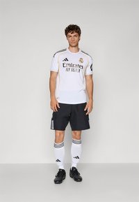 Bela nogometna majica s črnimi in zlatimi poudarki, črne kratke hlače, bele nogavice s črnimi črtami in črni kopački. Na njej sta logotip ekipe in sponzor.