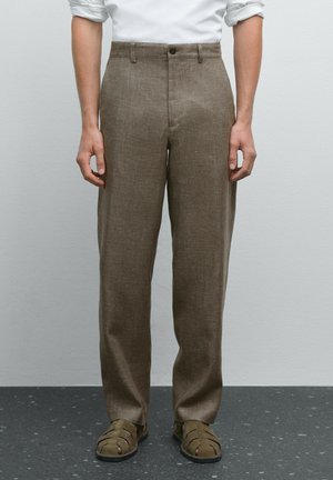 Brune linnedragt med lige snit, der har knaplukning og bæltestropper. Båret med beige sandaler på en grå overflade.