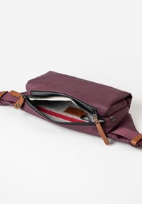 Borsa viola con un'esterno liscio, dotata di una chiusura a zip, manico in pelle e un interno foderato con accenti rossi.