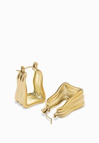 Kultaiset rengaskorvakorut, joissa on aaltoileva, veistoksellinen muotoilu. Varustettu kiiltävällä pinnalla ja saranaesiliimalla turvallisen istuvuuden takaamiseksi.