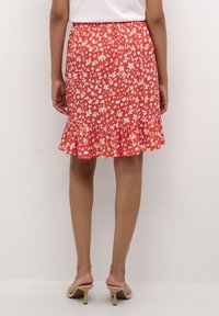 Jupe fleurie rouge avec des motifs blancs, taille élastique et ourlet froncé. Le tissu semble léger et lisse.