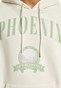 Felpa color crema con una grande stampa verde "PHOENIX" e un grafico circolare con il testo "Defining the Streets Since 2006" e "Ain't Definitely."