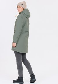 Olivgrön vattentät jacka med huva, texturerad tyg, dragkedja fram, sidofickor, kombinerad med grå jeans och svarta stövlar.