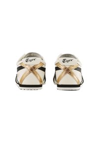White leather sneakers with gold accents and black stripes, featuring crisscross gold detailing on the heel and a textured white sole.