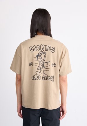 Kort beige t-skjorte med korte ermer, som har en leken grafikk på baksiden, med teksten "DICKIES" og "LAND AHOY!" i fet svart skrift.