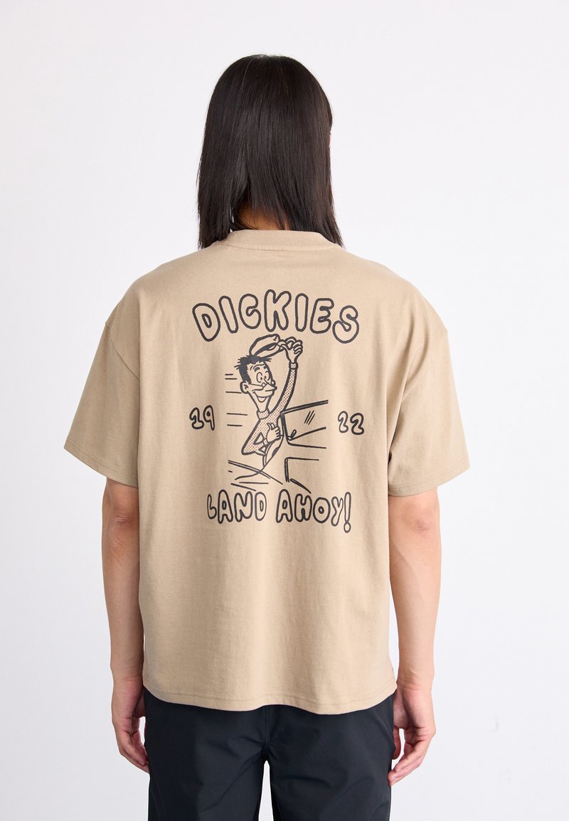 Trumpas smėlio spalvos marškinėliai trumpomis rankovėmis, ant nugaros esantis žaismingas grafikas su tekstu „DICKIES“ ir „LAND AHOY!“ paryškintu juodu šriftu.