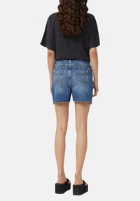 Shorts en denim bleu clair avec une hem effilée, cinq poches et une légère décoloration. Associés à un haut noir à manches courtes et des sandales noires épaisses.