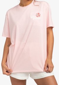 Camiseta oversized de color rosa claro, fabricada en algodón, con un diseño de bordado floral y el texto "Keep Smiling" en la zona del bolsillo del pecho.