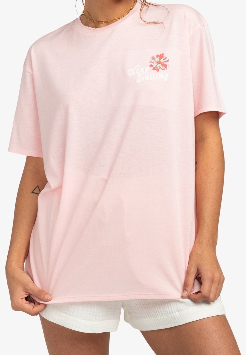 Camiseta oversized de color rosa claro, fabricada en algodón, con un diseño de bordado floral y el texto "Keep Smiling" en la zona del bolsillo del pecho.