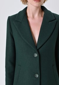 Blazer verde in lana con colletto a scollatura, chiusura con bottone a un solo petto e due tasche laterali. Materiale testurizzato con vestibilità su misura.