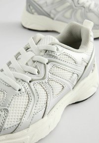 Witte sportieve sneaker met een combinatie van gestructureerd mesh en glad synthetisch materiaal. Bevat veters en een gevoerde zool met een zwart accent.